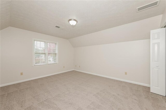 additional living space featuring light colored carpet, a textured ceiling, and vaulted ceiling
