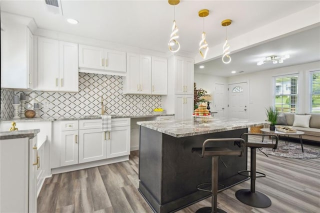 kitchen featuring decorative backsplash, light stone countertops, a center island, white cabinetry, and hardwood / wood-style flooring