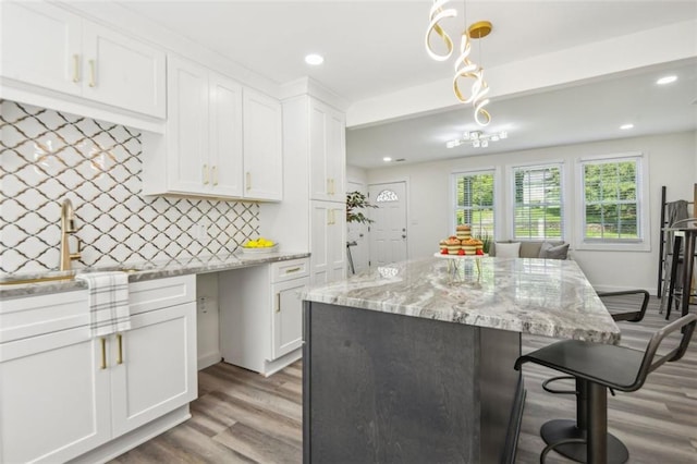 kitchen with white cabinets, backsplash, light stone counters, hardwood / wood-style floors, and decorative light fixtures