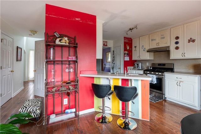 kitchen with white cabinets, dark hardwood / wood-style flooring, a kitchen bar, kitchen peninsula, and stainless steel gas range oven