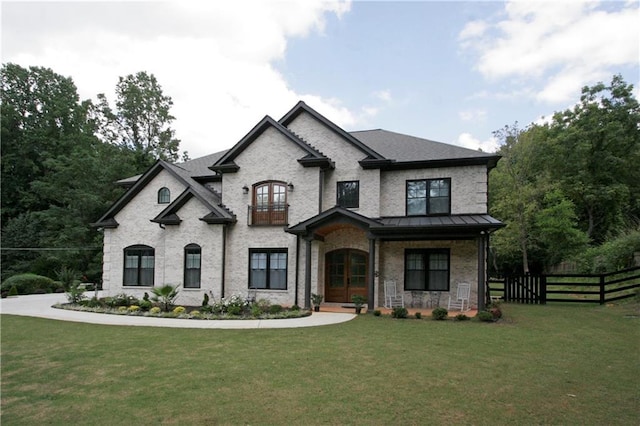 view of front of house with a balcony, brick siding, fence, a standing seam roof, and a front yard