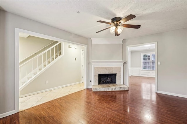 unfurnished living room with ceiling fan, hardwood / wood-style floors, a tile fireplace, and a textured ceiling