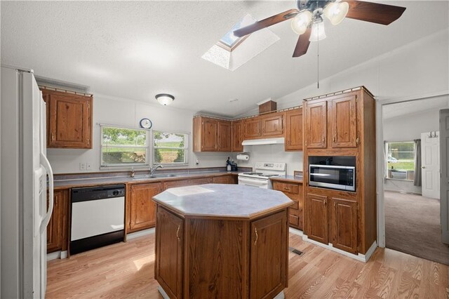 kitchen with white appliances, vaulted ceiling, a sink, light wood-style flooring, and a kitchen island