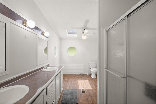 full bath with wood finished floors, a ceiling fan, a shower with shower door, toilet, and double vanity