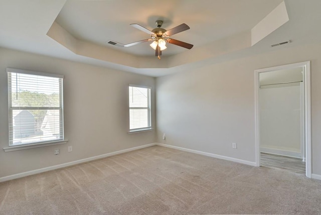 spare room with a raised ceiling, light colored carpet, and ceiling fan