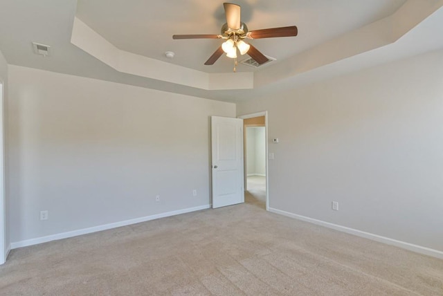 carpeted empty room with ceiling fan and a tray ceiling