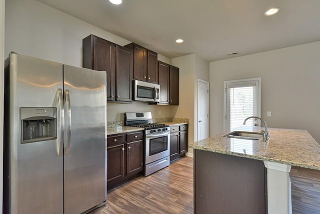 kitchen with sink, light stone counters, a center island with sink, stainless steel appliances, and hardwood / wood-style floors