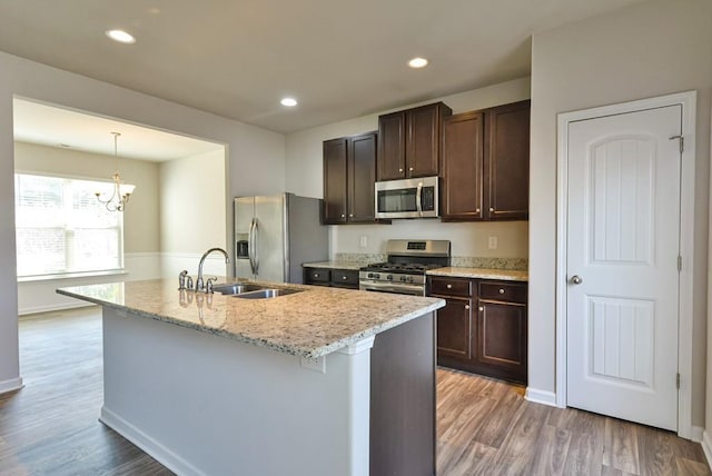 kitchen featuring appliances with stainless steel finishes, pendant lighting, wood-type flooring, sink, and a center island with sink