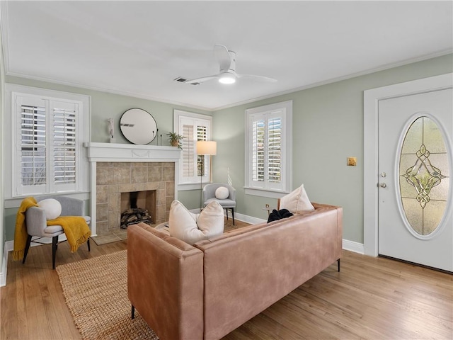 living room with a tile fireplace, crown molding, light hardwood / wood-style floors, and ceiling fan