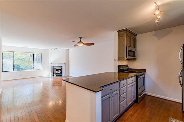 kitchen featuring dark stone countertops, dark hardwood / wood-style flooring, ceiling fan, kitchen peninsula, and stainless steel appliances