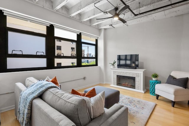 living room featuring a stone fireplace, wood-type flooring, and ceiling fan