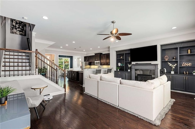 living room featuring crown molding, ceiling fan, stairway, and a fireplace