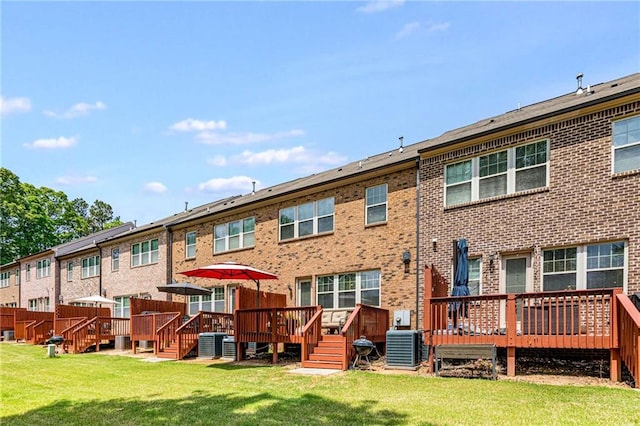 back of property with a lawn, a wooden deck, central air condition unit, and brick siding