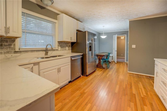 kitchen featuring stainless steel appliances, a sink, light wood finished floors, white cabinets, and a textured ceiling