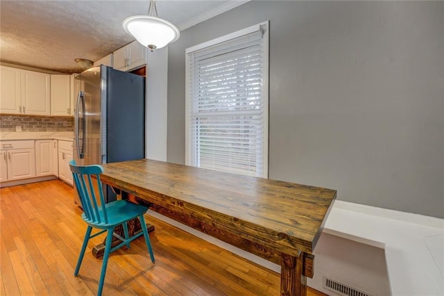 kitchen featuring appliances with stainless steel finishes, a textured ceiling, white cabinetry, ornamental molding, and light wood-style flooring