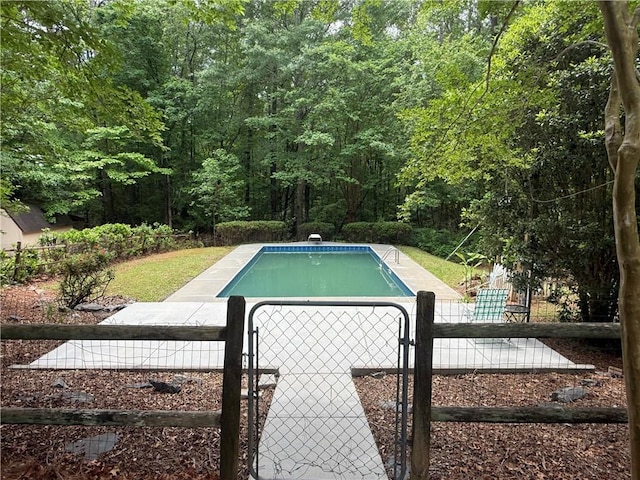 swimming pool with a gate, a wooded view, and fence