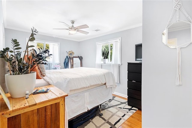 bedroom with multiple windows, light wood-style floors, crown molding, a ceiling fan, and baseboards
