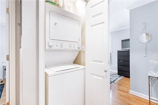 laundry area with stacked washer / dryer, light wood finished floors, ornamental molding, and baseboards