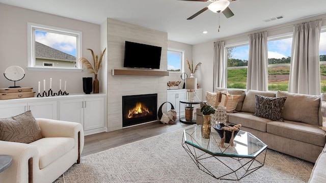 living area with visible vents, a tiled fireplace, light wood-style flooring, ceiling fan, and recessed lighting