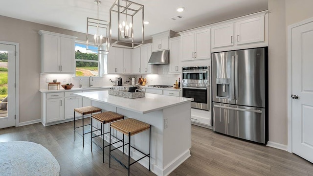 kitchen featuring a breakfast bar area, under cabinet range hood, a sink, appliances with stainless steel finishes, and decorative backsplash