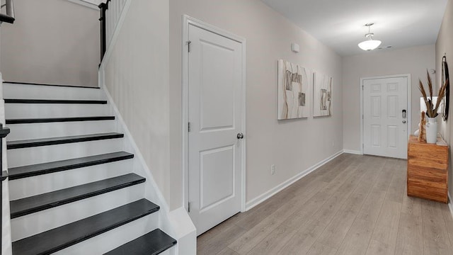 foyer entrance featuring light wood-style floors, baseboards, and stairs