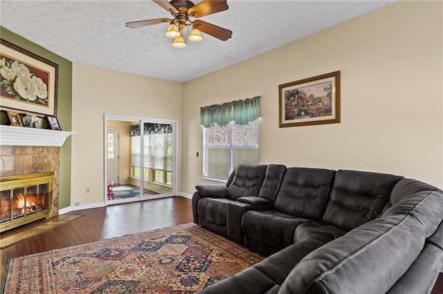 living area with baseboards, ceiling fan, a tiled fireplace, wood finished floors, and a textured ceiling