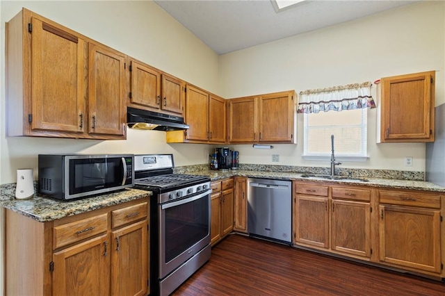 kitchen with dark wood-type flooring, light stone countertops, under cabinet range hood, stainless steel appliances, and a sink