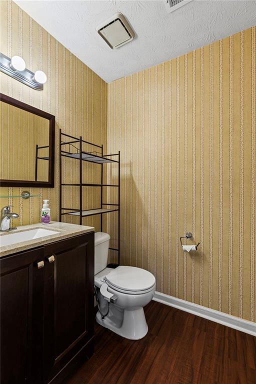 bathroom with toilet, wood finished floors, wallpapered walls, baseboards, and vanity