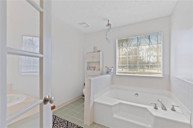 bathroom featuring vanity, a textured ceiling, a garden tub, toilet, and tile patterned floors