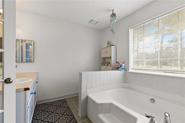 bathroom featuring a textured ceiling, tile patterned flooring, baseboards, a bath, and vanity