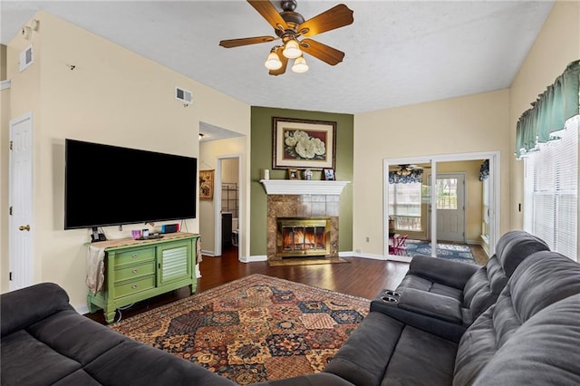 living room with dark wood-style floors, baseboards, visible vents, a tile fireplace, and ceiling fan