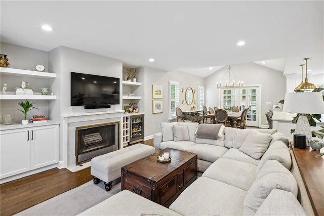 living room with built in features, an inviting chandelier, hardwood / wood-style floors, a high end fireplace, and vaulted ceiling