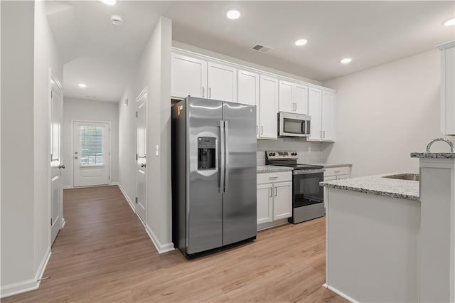 kitchen with light stone countertops, white cabinetry, stainless steel appliances, and light wood-type flooring