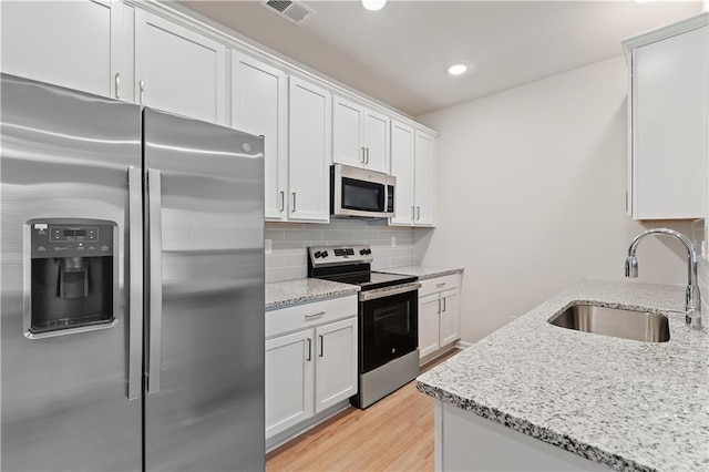 kitchen featuring white cabinets, appliances with stainless steel finishes, light stone counters, and sink