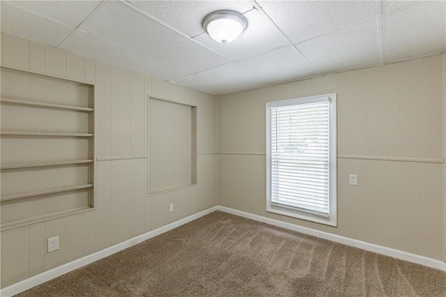 carpeted spare room with wood walls, a paneled ceiling, and built in shelves