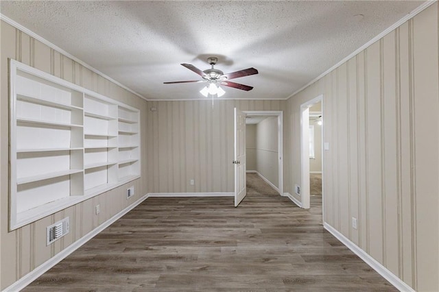 empty room featuring ornamental molding, wood-type flooring, a textured ceiling, and built in shelves