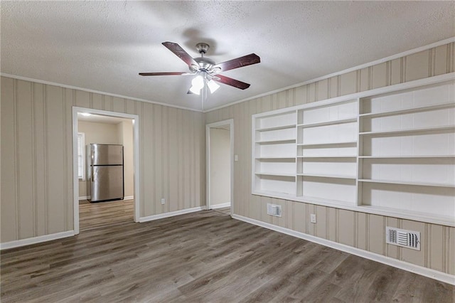 empty room featuring wood-type flooring, a textured ceiling, ceiling fan, crown molding, and built in shelves