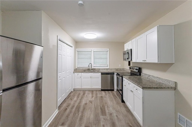 kitchen with appliances with stainless steel finishes, sink, white cabinetry, light hardwood / wood-style floors, and dark stone counters