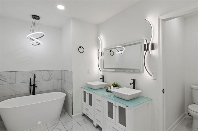 full bath featuring toilet, marble finish floor, a freestanding tub, and a sink