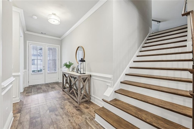 foyer with wood finished floors, a wainscoted wall, visible vents, ornamental molding, and french doors