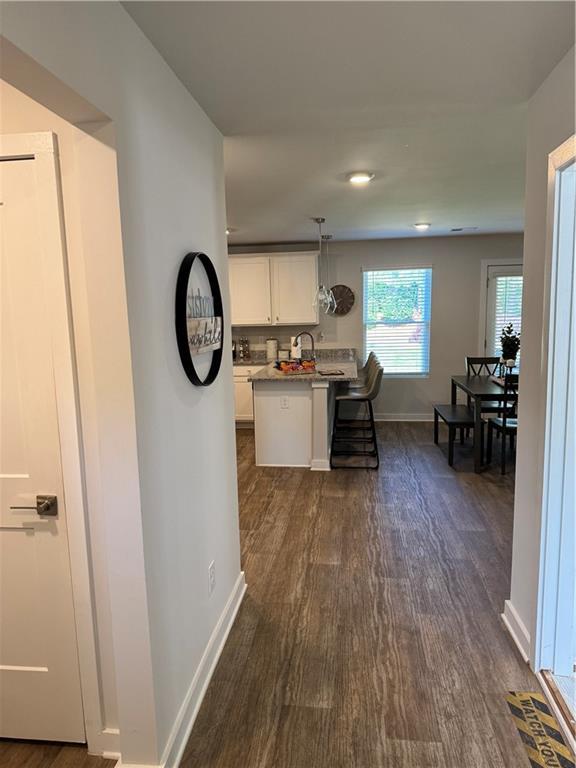 719 Windstream Dr, Lagrange, GA 30241 - kitchen with dark wood-type flooring, white cabinets, baseboards, a breakfast bar area, and light countertops