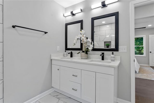 ensuite bathroom featuring marble finish floor, a sink, baseboards, and double vanity