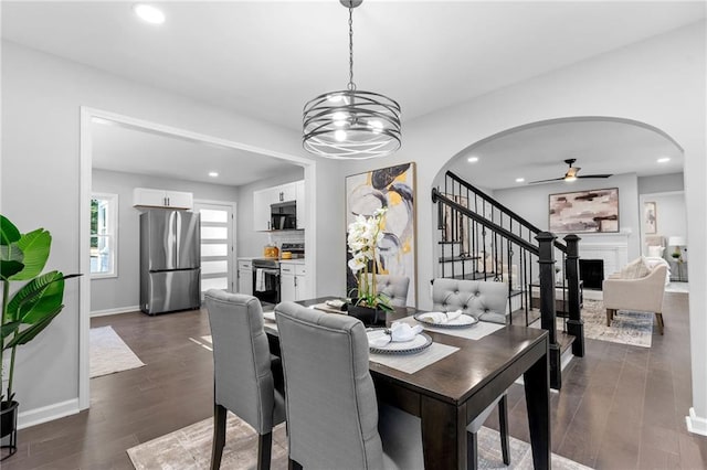 dining space with arched walkways, a brick fireplace, dark wood finished floors, and recessed lighting