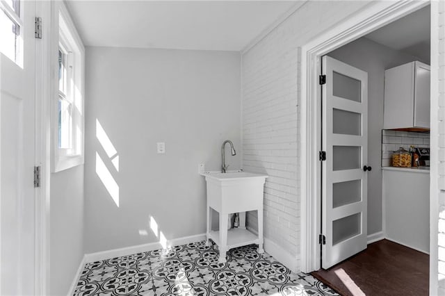 clothes washing area featuring baseboards and brick wall