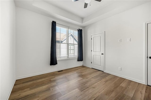 unfurnished room with baseboards, a raised ceiling, and wood finished floors