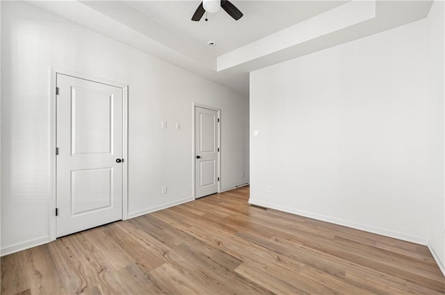 unfurnished room with ceiling fan, light hardwood / wood-style floors, and a tray ceiling