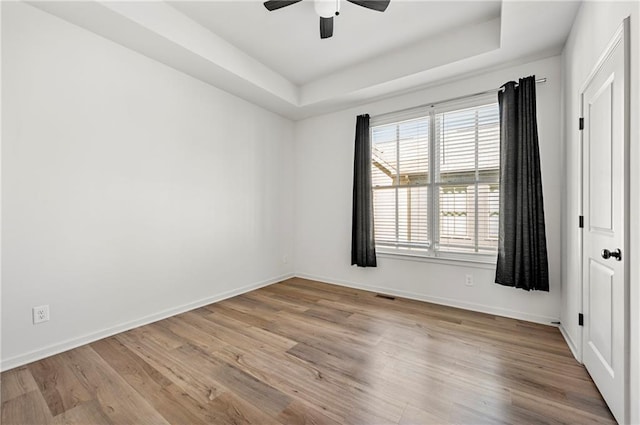 spare room featuring a tray ceiling, wood finished floors, and baseboards