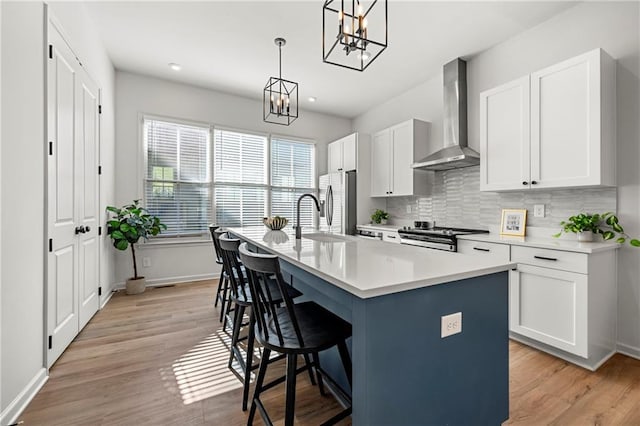 kitchen with white cabinetry, wall chimney exhaust hood, stainless steel appliances, and a center island with sink