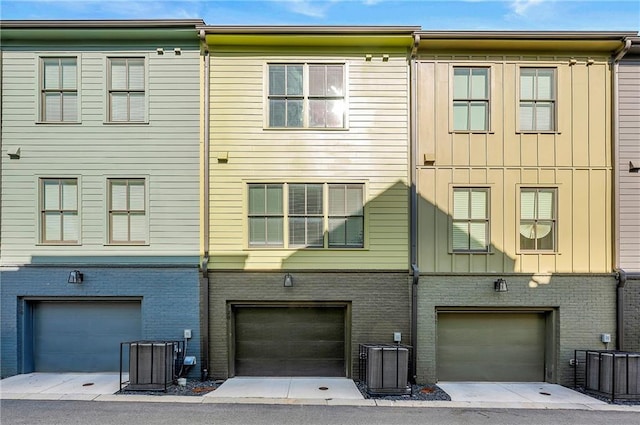 rear view of property with an attached garage, central AC unit, and brick siding