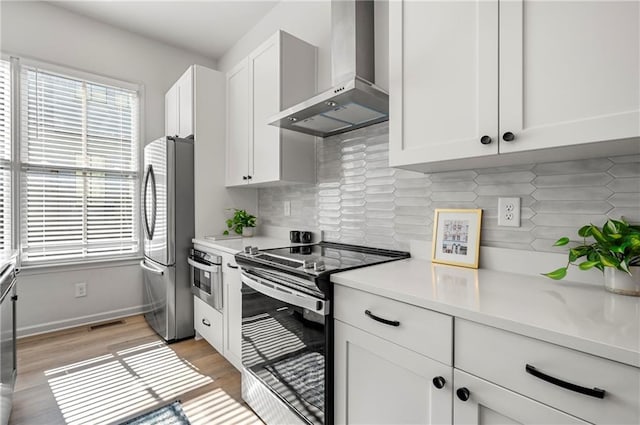 kitchen featuring stainless steel appliances, light countertops, white cabinets, wall chimney exhaust hood, and light wood-type flooring